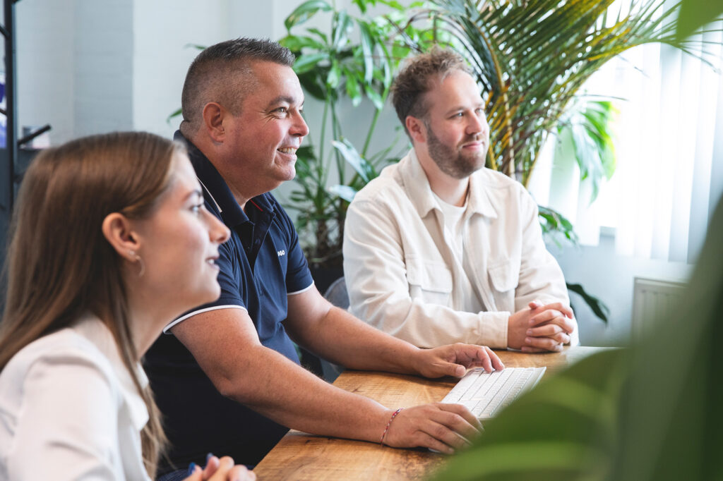 Teamleden van Marker Media werken samen tijdens een creatieve bespreking in een groene kantooromgeving.