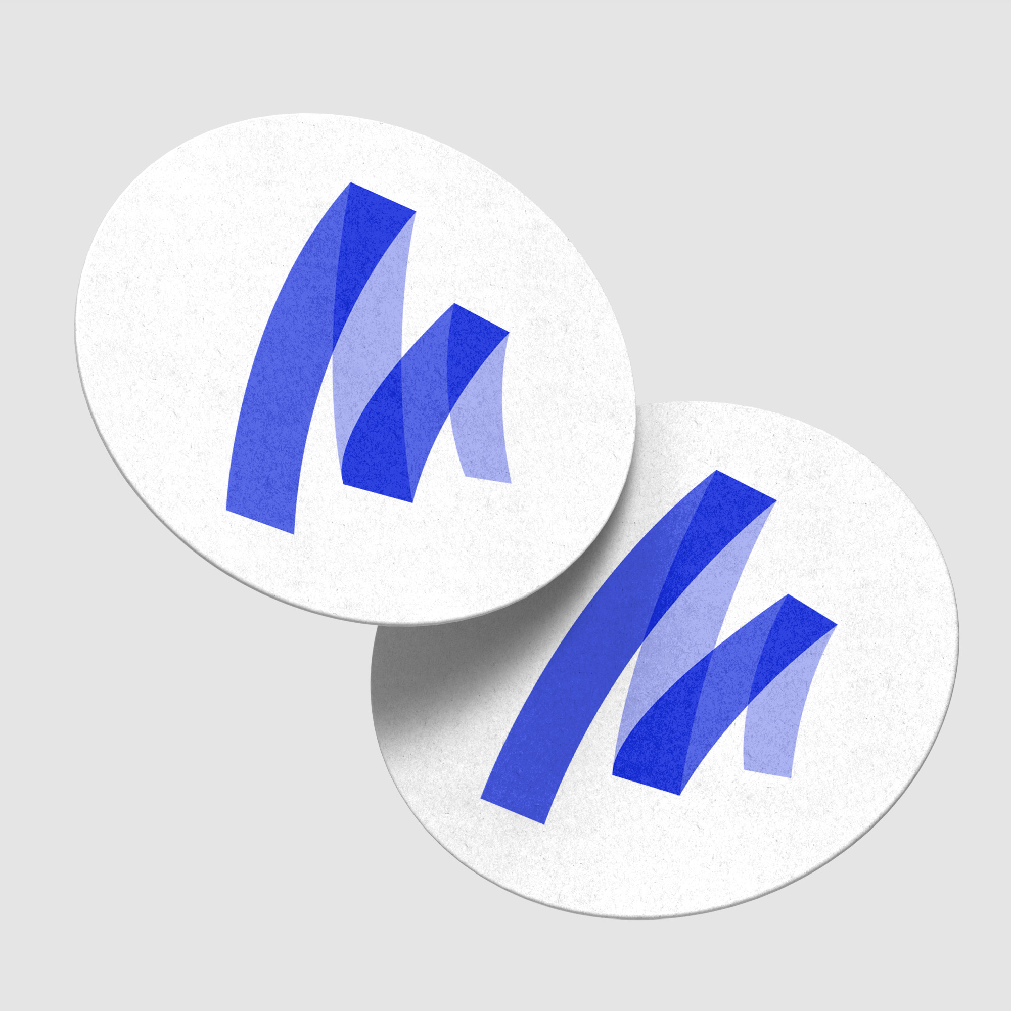 Twee ronde bierviltjes met het blauwe logo van reclamebureau Marker Media op een grijze achtergrond.